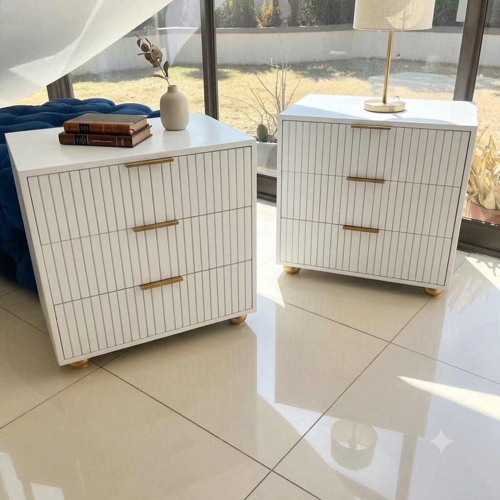 White ribbed pedestal drawers with gold bar handles and gold ball feet, styled in a bright modern bedroom