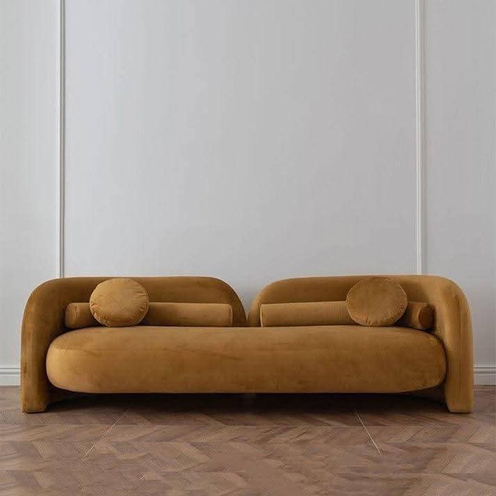 Ochre velvet organic arch sofa with rounded tubular arms and matching bolster cushions against a white wall